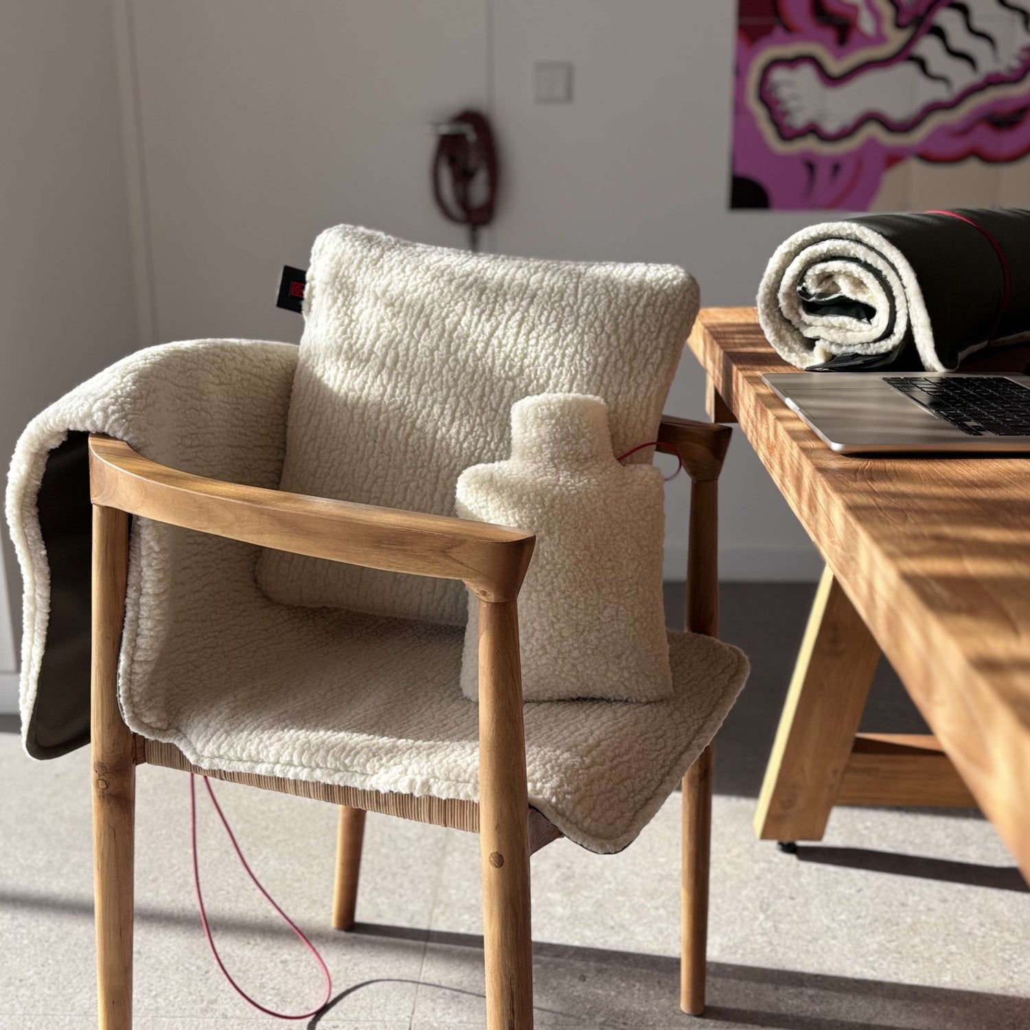 Plaid, coussin et bouillotte Sukha en laine de brebis recyclée, posés sur une chaise dans un intérieur chaleureux